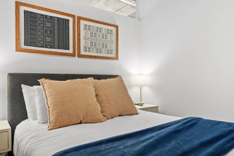 Cozy bedroom with a grey upholstered headboard, oversized pillows, and decorative wall art.
