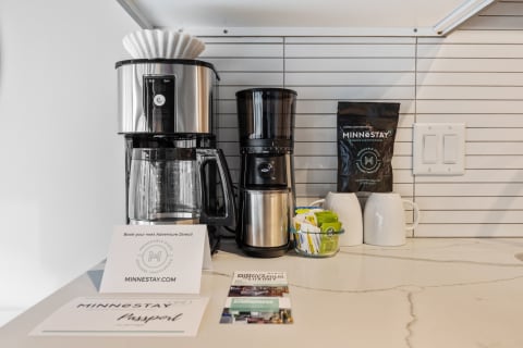 A drip coffee maker and grinder set up on a countertop with promotional materials for MINNESTAY.
