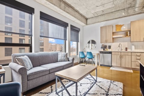 Modern living area featuring a gray sofa, coffee table, and kitchen space.