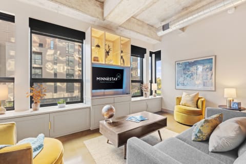 A contemporary living area with a gray sofa, yellow accent chair, coffee table, and large windows.