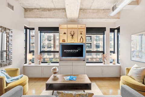 A modern living room featuring a gray sofa, yellow accent chair, wooden coffee table, and decorative shelving unit with a TV.
