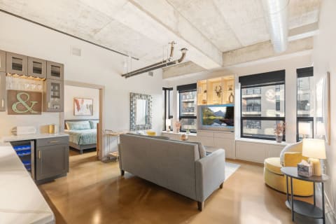 Interior of a modern studio apartment with a gray sofa, yellow accent chair, and kitchenette.
