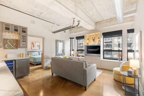A stylish studio apartment featuring a gray sofa, yellow accent chair, and a modern kitchenette.