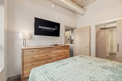Modern bedroom with a wooden dresser, wall-mounted TV, and sliding doors to a bathroom.