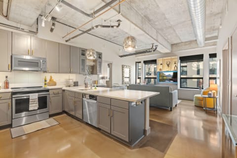 Modern kitchen with gray cabinetry, white countertop, and open living area featuring a light gray sofa.