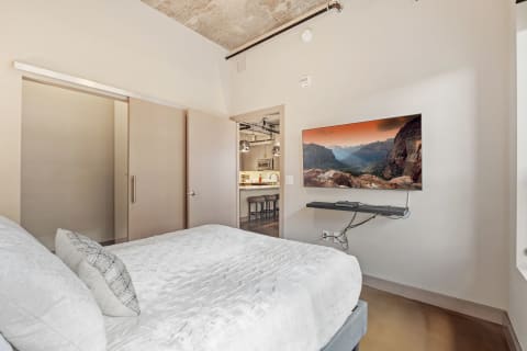 A clean modern bedroom featuring a large bed and a flat-screen TV showing a scenic landscape.