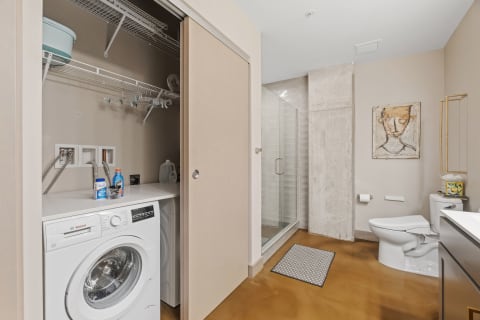 Interior view of a modern bathroom with a washing machine, shower, and toilet.