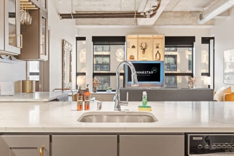 A modern kitchen with a white marble countertop and a cozy living room in the background.