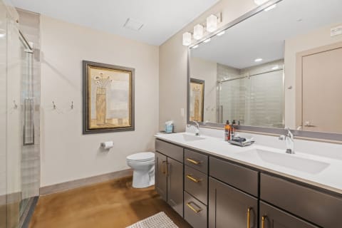 Modern bathroom with glass shower, dual sinks, and art piece on the wall.
