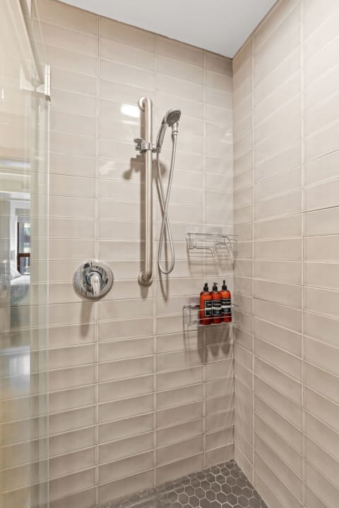 Modern shower with beige tiles, chrome fixtures, and products on a shelf.