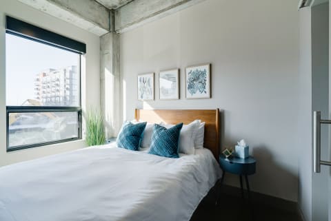 A beautifully arranged bedroom featuring a made bed, abstract art, and a modern side table.