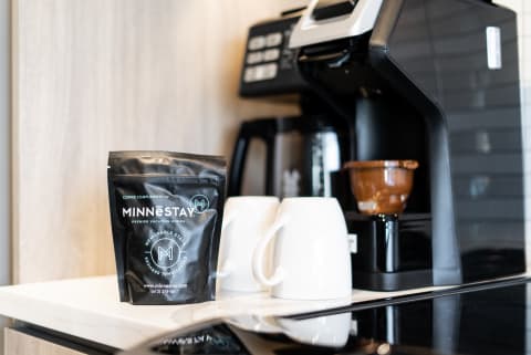 A coffee bag from Minnestay beside white mugs and a coffee maker on a counter.