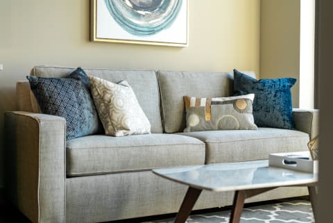 A gray sofa with decorative pillows next to a coffee table and artwork on the wall.