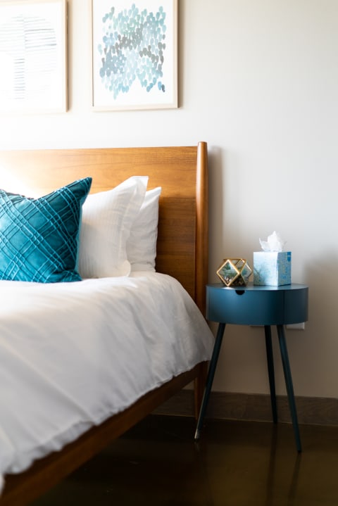 Cozy bedroom corner with wooden bed, teal pillow, and decorative bedside table.