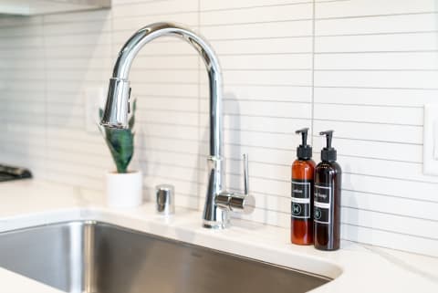 Contemporary kitchen sink featuring a chrome faucet and skincare product bottles.