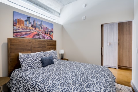 Interior view of a modern bedroom featuring a double bed with patterned bedding and cityscape art.