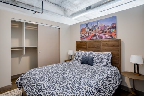 A modern bedroom with a patterned duvet, wooden headboard, city skyline artwork, and minimal decor.