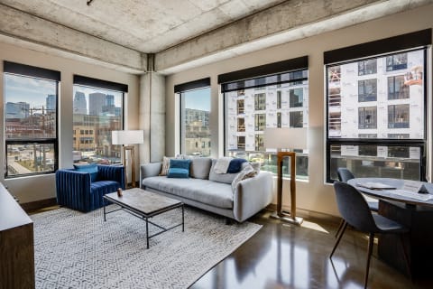 Contemporary living room with large windows and city view, featuring a gray sofa and blue accent chair.