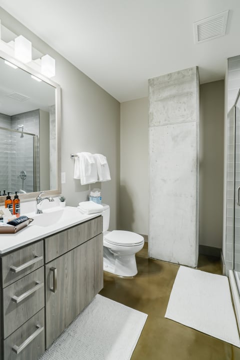 Sleek and modern bathroom with gray vanity, white towels, and a glass shower.