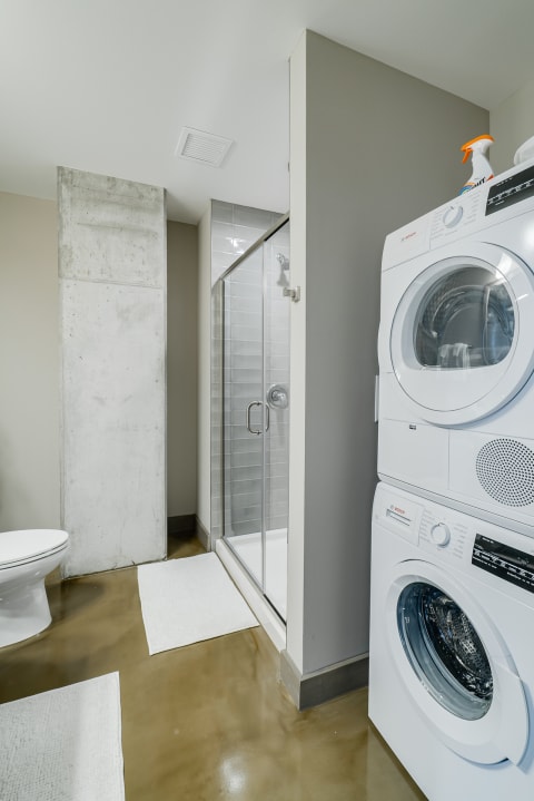 Modern bathroom with a shower, a white toilet, and a stacked washer and dryer.