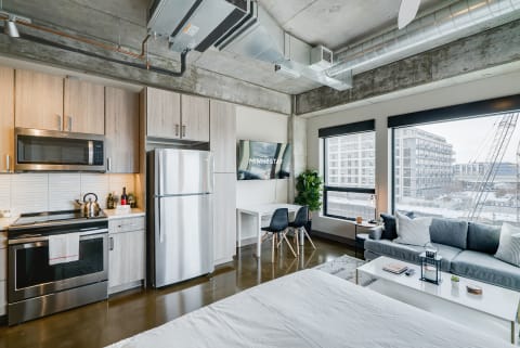 A modern studio apartment featuring a kitchen, living area, and dining space with large windows.