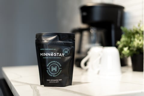 A bag of MINNESTAY coffee sits on a kitchen counter next to a coffee maker and white cups.