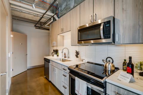 A contemporary kitchen featuring light wooden cabinets, stainless steel appliances, and white countertops.