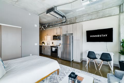 Interior view of a modern studio apartment featuring a bed, kitchen area, and a TV.