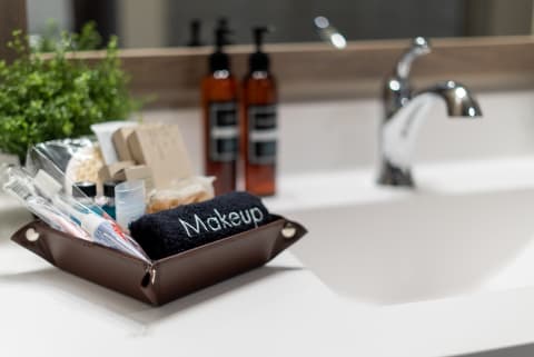 Organized bathroom countertop featuring a brown tray with makeup items and a towel, complemented by shampoo bottles and a potted plant.