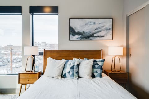 Modern bedroom with a cozy bed, geometric pillows, and large windows overlooking a cityscape.