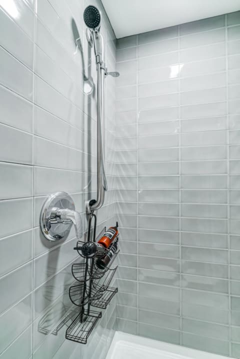 A modern shower with gray tiles, chrome fixtures, and a shower caddy holding bottles.