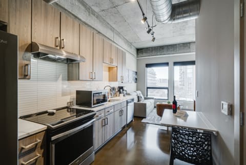 Modern apartment kitchen featuring light wood cabinetry and a cozy living area with a gray sofa.