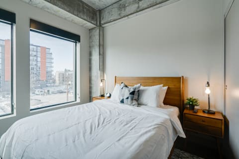 Modern bedroom with a wooden bed and large windows overlooking an urban landscape.
