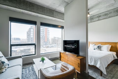 Contemporary studio apartment interior with a living area and bedroom, large windows showing cityscape.