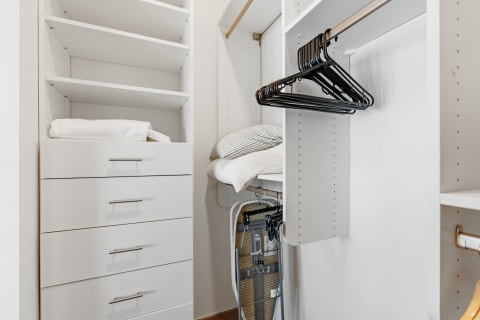 Interior of a contemporary closet featuring white shelves, a set of drawers, and black hangers.