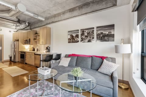 Stylish modern apartment interior with a gray couch, kitchenette, and city skyline artwork.