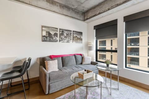 Cozy living area with gray sofa, glass tables, and city skyline artwork.
