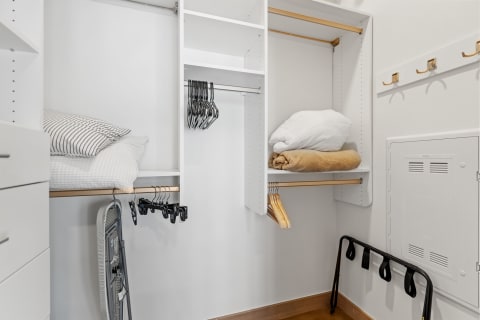 Neatly organized closet with pillows, blankets, hangers, and an ironing board.
