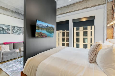 Modern bedroom with a bed, sofa, TV, and urban view windows.