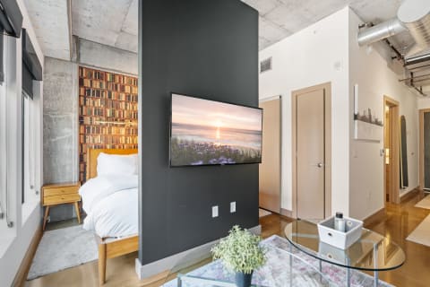 Modern studio apartment with a dark accent wall and a serene beach sunset on the TV.
