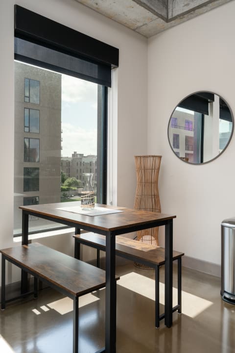 Modern dining area with a wooden table, benches, and a decorative vase in a sunlit room.