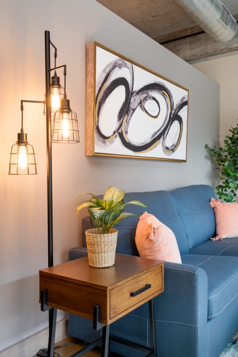 A corner of a modern living room with a blue sofa, abstract painting, side table, and floor lamp.