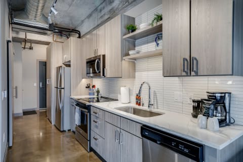 Modern kitchen featuring light wood cabinets, stainless steel appliances, and marble countertops.