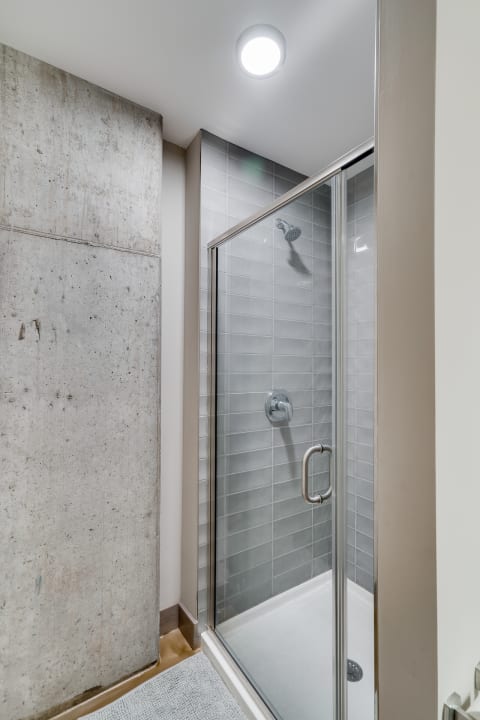 A modern shower featuring a glass enclosure and gray tiled walls next to an unfinished concrete wall.