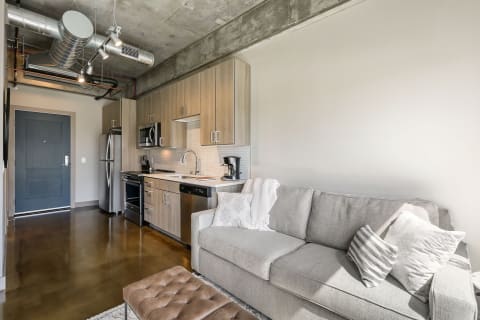 Interior view of a modern studio apartment with a gray sofa, kitchen appliances, and polished concrete floor.