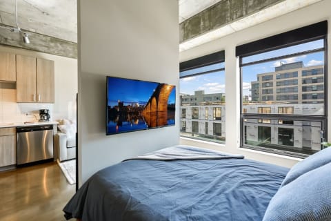 Modern studio apartment with a view of the city skyline and a kitchenette.