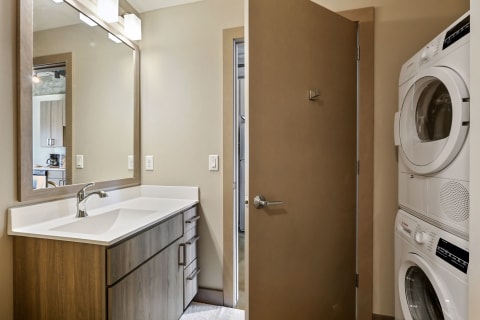 Modern bathroom with a sink, mirror, and adjacent laundry appliances.