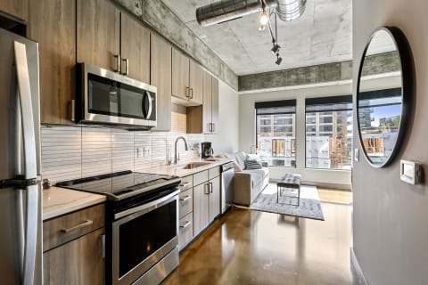 Modern kitchen and living area with stainless steel appliances, sleek cabinetry, and urban views through windows.
