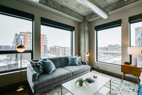A contemporary living room with a grey sofa, large windows, and winter city views.