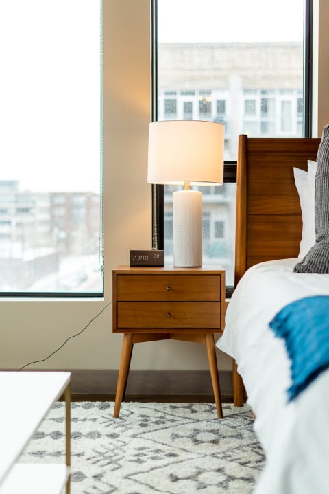 Cozy bedroom corner featuring a wooden nightstand with a lamp and clock, beside a made bed.